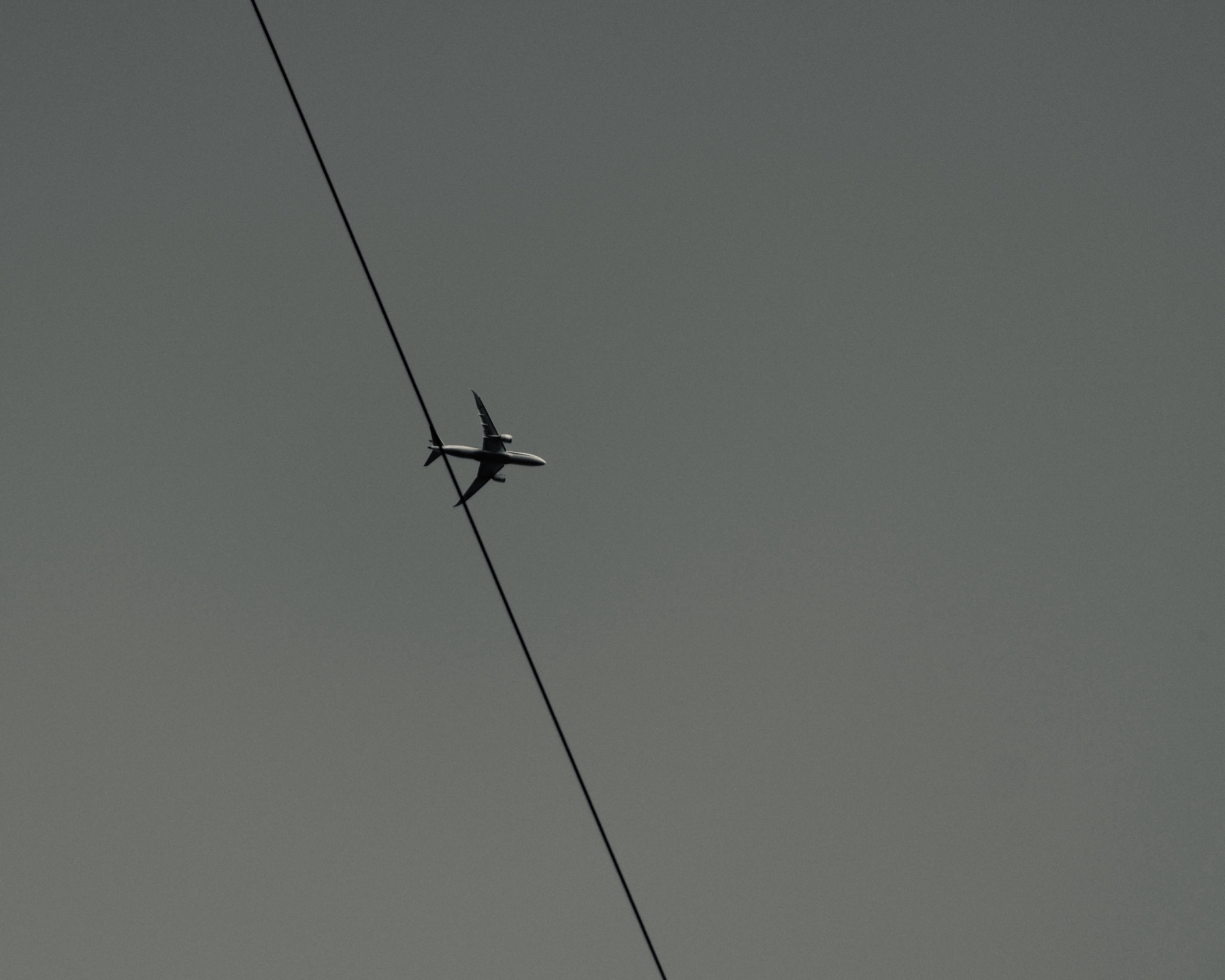 Airplane crossing power line against gray sky